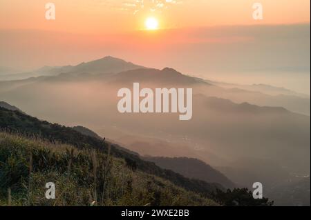 Il sole al tramonto proietta un velo di nebbia in vivaci sfumature arancioni, creando un ampio arazzo di colore sulla montagna. Buyan Pavilion, New Taipei City. Foto Stock