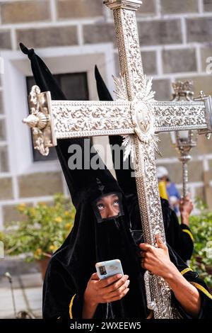 Antigua, Guatemala. 29 marzo 2024. Un membro di una confraternita di penitenti, indossando cappelli capirote, controlla il suo cellulare mentre aspetta fuori dalla chiesa Escuela de Cristo per l'inizio della processione del venerdì Santo del Senor Sepultado durante la Semana Santa, 29 marzo 2024 ad Antigua, Guatemala. L'opulenta processione è una delle più grandi al mondo, coinvolgendo migliaia di devoti e durando 12 ore. Crediti: Richard Ellis/Richard Ellis/Alamy Live News Foto Stock
