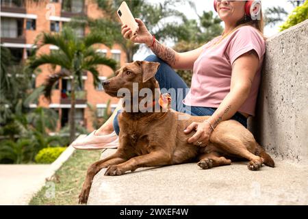 Primo piano di un bellissimo cane dalla pelliccia marrone con una bandana arancione e un bindi sulla fronte, accompagnato dal proprietario seduto accanto a lei. Foto Stock