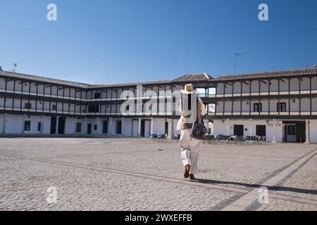 Da sotto, una donna anonima di mezza età viaggiatrice con un giubbotto e un cappello da cowboy, camminando su una piazza storica. In Plaza Mayor di Tembleque a Toledo Foto Stock