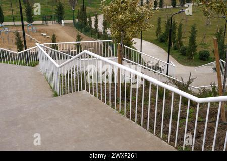 Una lunga scalinata curva con ringhiere in metallo bianco scende in una verdeggiante area del parco. Foto Stock