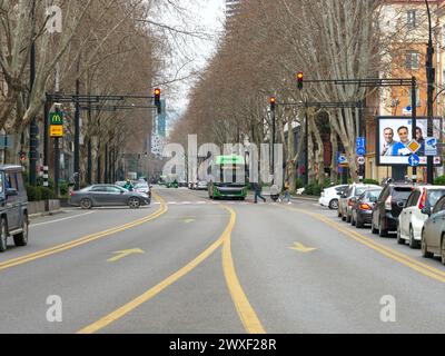 Una vivace e moderna strada cittadina con autobus verdi, auto e pedoni, che suggeriscono movimento e attività urbana. Tbilisi, Georgia - 27 febbraio 2024. Foto Stock