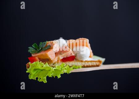 pane tostato fritto con salmone, formaggio spalmabile, insalata, isolato su sfondo nero Foto Stock