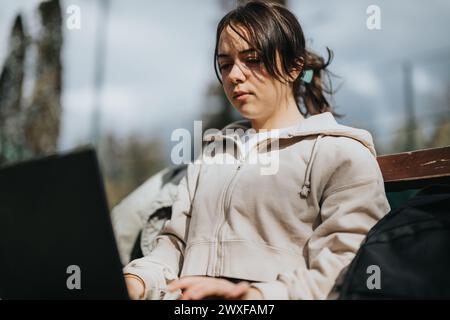 Giovane ragazza spensierata che usa un notebook mentre è seduta in un parco durante il fine settimana Foto Stock