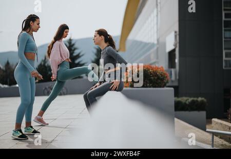 Tre donne atletiche che si allungano prima di un allenamento in un ambiente urbano Foto Stock