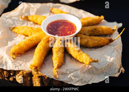 Spiedini di pollo fritti in profondità dorati e croccanti serviti con una salsa piccante di peperoncino dolce su carta rustica e sfondo di legno. Foto Stock