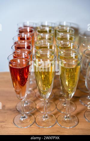 File di champagne frizzante a flauti, con sfumature dorate e rosa, disposte su un tavolo di legno per una festa. Foto Stock