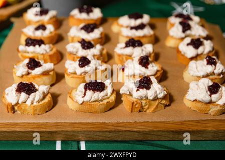 Bruschette tostate con crema di formaggio montata, tonno e cipolla rossa caramellata, disposte su un asse di legno. Foto Stock