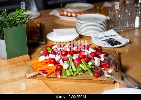 Un vivace vassoio di crudité con una vasta gamma di verdure fresche, tra cui ravanelli, pomodori ciliegini e carote, ordinate su un asse di legno. Foto Stock