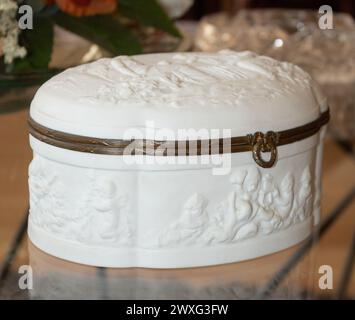 Cassettiera in ceramica bianca con angeli ricamati e bordi in legno marrone sulla parte superiore di un tavolo in vetro Foto Stock