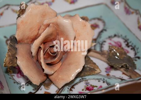 Fiore rosa in ceramica lucente su un piatto delicato e femminile di tè chiaro con decorazioni di fiocchi e fiori su sfondo in legno Foto Stock