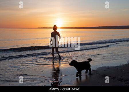 Portobello, Edimburgo, Scozia, Regno Unito. 31 marzo 2024. Splendida alba per il benvenuto nel periodo estivo britannico sul mare scozzese, così come la domenica di Pasqua. Nella foto: Makiko Konishi fa un tuffo fresco nel Firth of Forth all'alba mentre il suo cockapoodle Renzo aspetta sulla riva, temperatura di 6 gradi centigradi. Credito: Arch White/alamy notizie dal vivo. Foto Stock
