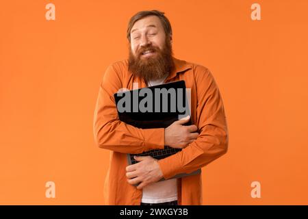 Happy Redhaired Bearded Man abbraccia il suo computer portatile, Orange Studio Foto Stock