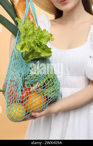 Donna con un sacchetto di verdure fresche e baguette su sfondo beige, primo piano Foto Stock