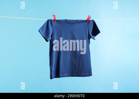 Una t-shirt che si asciuga sulla linea di lavaggio su sfondo azzurro Foto Stock