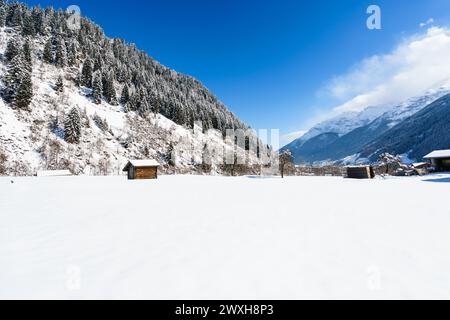 Montagne innevate, campi e cabine contro un cielo azzurro limpido in inverno Foto Stock