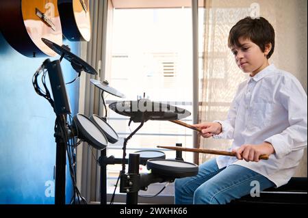 Ritratto autentico di un bellissimo adolescente caucasico che batte con le bacchette sui piatti mentre esegue il suono sulla batteria, suonando la musica Foto Stock