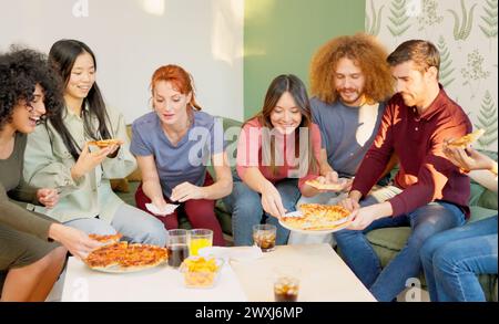 Amici che si rilassano e sorridono mangiando la pizza insieme a casa Foto Stock