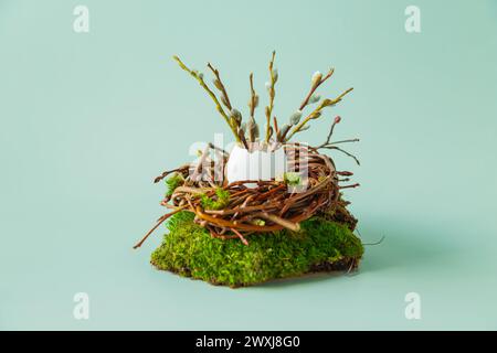 Uova di quaglia, piume e rami di salice in un nido su sfondo azzurro. Sfondo pasquale con spazio di copia per il testo. Foto Stock