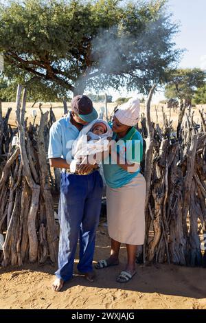 padre e madre africani con un bambino nel villaggio di fronte alla cucina all'aperto, un'organizzazione no-profit che aiuta Foto Stock