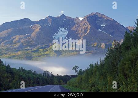 Le strade prive di traffico portano in pendenza verso montagne accidentate e innevate, nebbia mattutina in autunno, Richardson Highway, Alaska, Stati Uniti Foto Stock