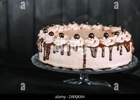 Primo piano di una deliziosa torta al cioccolato con ganache al cioccolato su un banco per torte di vetro. La torta è posta su un tavolo di legno scuro Foto Stock