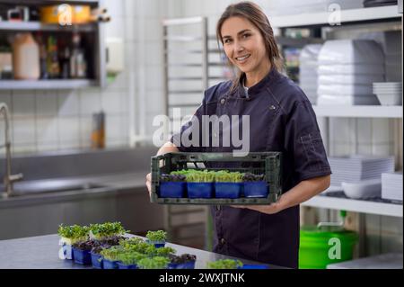 Donna in uniforme che tiene i microgreen nella cucina del ristorante Foto Stock