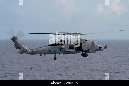 SOUTH CHINA SEA (27 marzo 2024) un MH-60R Sea Hawk, assegnato al "Wolf Pack" dell'Helicopter Maritime Strike Squadron (HSM) 75, si avvicina alla portaerei classe Nimitz USS Theodore Roosevelt (CVN 71), 27 marzo 2024. La Theodore Roosevelt, nave ammiraglia del Carrier Strike Group Nine, sta conducendo operazioni di routine nell'area delle operazioni della 7th Fleet. La U.S. 7th Fleet è la più grande flotta numerata della Marina degli Stati Uniti, e interagisce e opera regolarmente con alleati e partner nel preservare una regione indo-pacifica libera e aperta. (Foto della Marina degli Stati Uniti di Mass Communication Specia Foto Stock