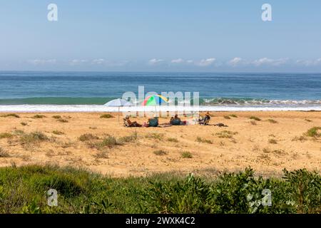 Gli amici si siedono da soli e si rilassano sotto gli ombrelloni a Newport Beach a Sydney, Australia, ammirando la vista dell'oceano e dell'orizzonte, 2024 Foto Stock