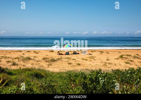 Gli amici si siedono da soli e si rilassano sotto gli ombrelloni a Newport Beach a Sydney, Australia, ammirando la vista dell'oceano e dell'orizzonte, 2024 Foto Stock