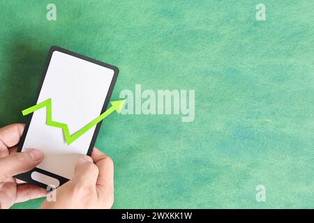 Mano maschile che tiene un telefono cellulare con la freccia verde rivolta verso l'alto. Recupero, mobile trading e crescita. Foto Stock