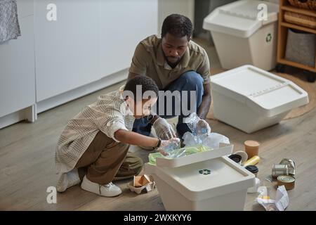 Ritratto ad alto angolo di padre e figlio che smistano insieme i rifiuti domestici e collocano bottiglie di plastica nello spazio di copia dei contenitori Foto Stock