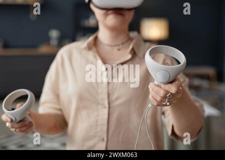 Foto selettiva di una giovane donna irriconoscibile che indossa un visore VR con controller che gioca ai videogame Foto Stock