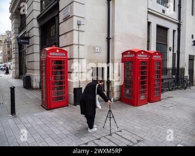 Londra, Regno Unito - 26 febbraio 2024: Una giovane donna prepara il suo smartphone per scattare un selfie con le famose cabine telefoniche rosse di Londra Foto Stock