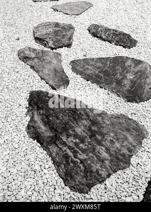 Le lastre di granito nero tagliate in forme libere sono state disposte per decorare il passaggio su un pavimento di ciottoli bianchi. Primo piano di pietra Foto Stock