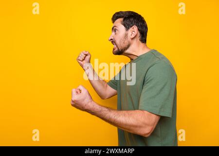 Foto ritratto di un bel giovane ragazzo che solleva i pugni reazione infastidita indossare abiti cachi alla moda isolati su sfondo giallo Foto Stock