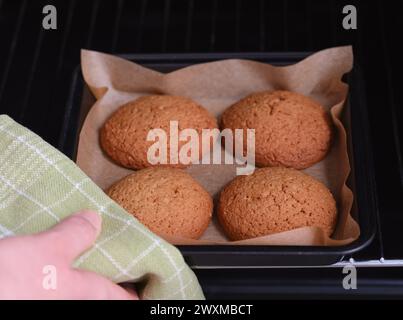 Una donna che prende un vassoio da forno con quattro biscotti d'avena. Foto Stock