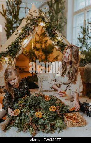 Una ragazza e una donna che decorano una corona di Natale con fette d'arancia Foto Stock