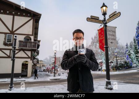 Young Man che controlla il telefono in Snowy Winter Scene Foto Stock