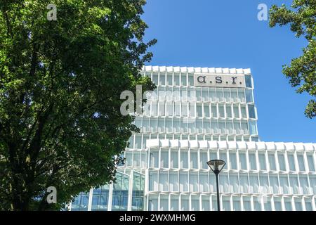 Moderno edificio per uffici con facciata in vetro e logo aziendale sotto il cielo azzurro e circondato da alberi frondosi verdi Foto Stock