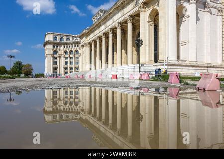 L'architettura neoclassica del Palazzo del Parlamento di Bucarest in Romania si riflette in una pozzanghera sul marciapiede Foto Stock