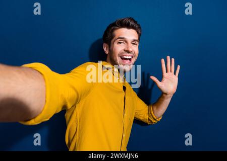 Foto ritratto di un giovane uomo scattate un selfie indossando un abito giallo alla moda isolato su sfondo blu scuro Foto Stock