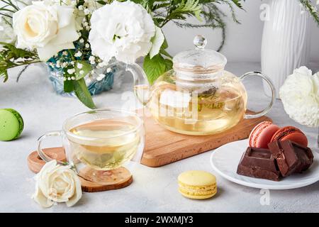 Tavolo estetico mattutino. Teiera, tazza, dessert di macaroon, cioccolato, fiori bianchi - tempo per te stesso, goditi il tuo concetto di tempo. Foto Stock