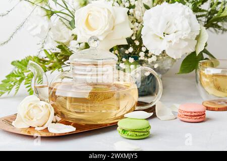 Mattinata estetica. Tè verde, dessert ai macaroon, sfondo bianco per lo stile di vita al bouquet. Tempo femminile di meditazione per te stesso, concetto di vita lenta Foto Stock