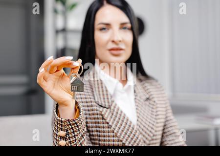 Giovane donna sorridente che tiene le chiavi di una nuova casa o di un appartamento. Affittuaria o affittuaria felice che festeggia il trasferimento a casa propria. Concetto di noleggio Foto Stock
