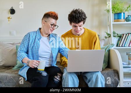 Madre e figlio di 19-20 anni, seduti insieme sul divano di casa, guardando lo schermo del notebook Foto Stock