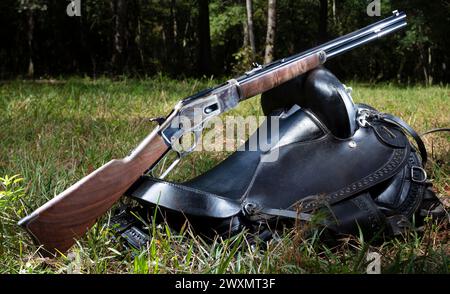 Fucile a leva in stile cowboy appoggiato su una sella in una foresta verde. Foto Stock