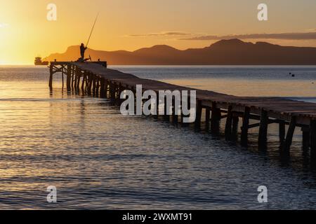 Pescatore sul molo di legno all'alba nella baia di Port d'Alcudia a Maiorca Foto Stock