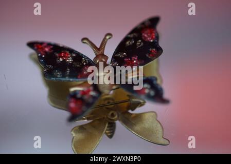 Una spilla colorata a farfalla arroccata su sfondo rosa con sfumature scure Foto Stock