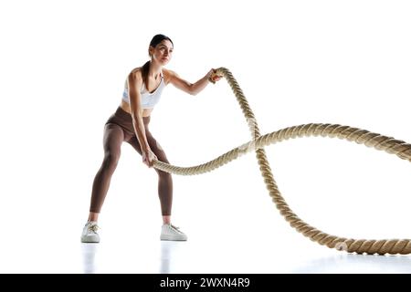 Giovane donna in forma forte che fa esercizi con corde da battaglia in palestra su sfondo bianco studio. Foto Stock